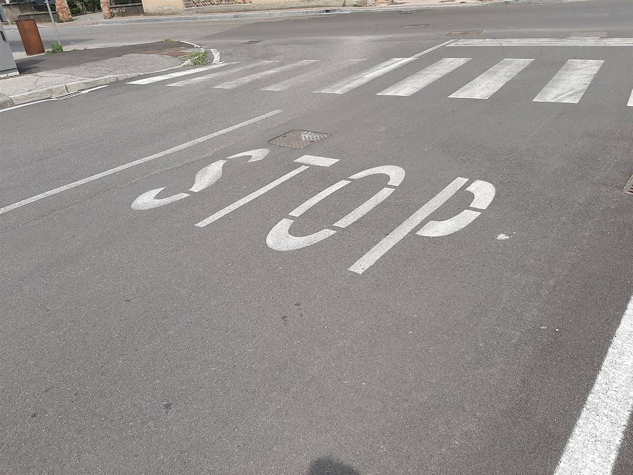Scritta STOP e strisce pedonali dipinte sull’asfalto di una strada urbana, con la vernice in parte consumata
