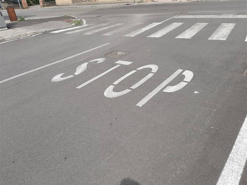 Scritta STOP e attraversamento pedonale dipinti sull’asfalto di una strada urbana, con la vernice in parte consumata